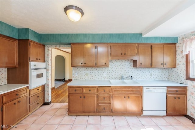 3817 Washington Park Blvd, Newburgh Heights, OH 44105 - kitchen featuring white appliances, arched walkways, wallpapered walls, brown cabinets, and light countertops