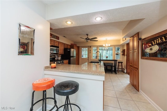 11756 Clarke Rd, Columbia Station, OH 44028 - kitchen featuring appliances with stainless steel finishes, light tile patterned floors, a peninsula, brown cabinets, and a chandelier