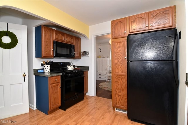 3921 Grosvenor Rd, South Euclid, OH 44118 - kitchen featuring black appliances, light wood finished floors, dark countertops, arched walkways, and brown cabinetry