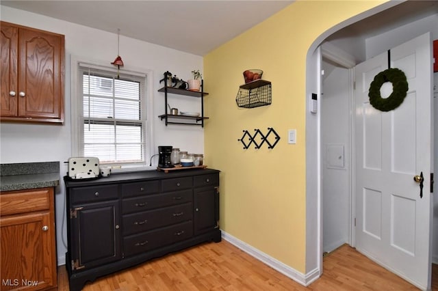 3921 Grosvenor Rd, South Euclid, OH 44118 - kitchen featuring arched walkways, light wood-style flooring, dark countertops, brown cabinetry, and open shelves