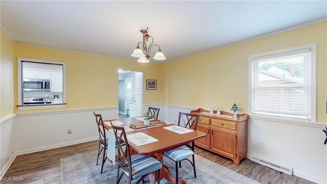 87 Holcomb Ave, Mogadore, OH 44260 - dining space with light wood finished floors, ornamental molding, wainscoting, a baseboard radiator, and a chandelier