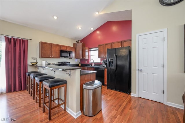 4504 Ledge Ct, Kent, OH 44240 - kitchen with black appliances, a breakfast bar, a peninsula, dark countertops, and light wood-type flooring