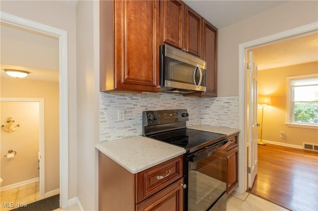 29504 Cresthaven Dr, Willowick, OH 44095 - kitchen featuring black electric range, stainless steel microwave, decorative backsplash, light stone counters, and light wood finished floors