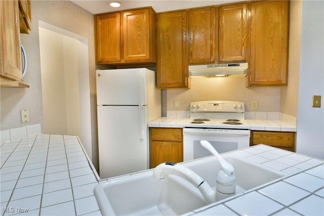 106 N Aspen Ct Unit 4, Warren, OH 44484 - kitchen with white appliances, under cabinet range hood, tile counters, and brown cabinetry