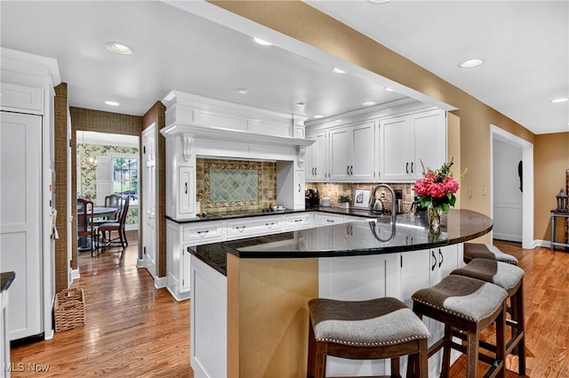335 N Union Ave, Salem, OH 44460 - kitchen featuring a peninsula, light wood-style flooring, white cabinetry, backsplash, and a breakfast bar area