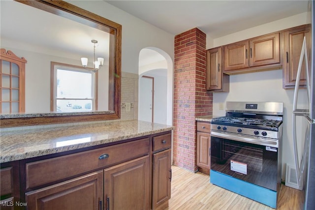 8102 Bertha Ave, Parma, OH 44129 - kitchen featuring stainless steel appliances, light stone counters, light wood finished floors, arched walkways, and a chandelier