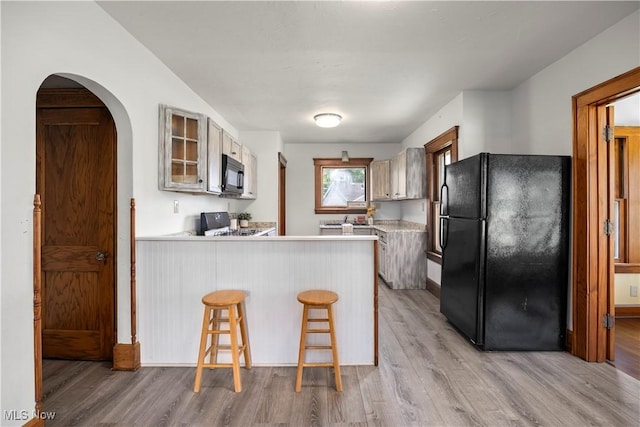1029 S Main St, Grafton, OH 44044 - kitchen with black appliances, light wood-style floors, a peninsula, glass insert cabinets, and light countertops