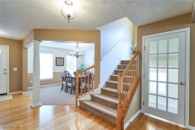 entrance foyer featuring ornate columns, light wood finished floors, stairway, a chandelier, and a textured ceiling