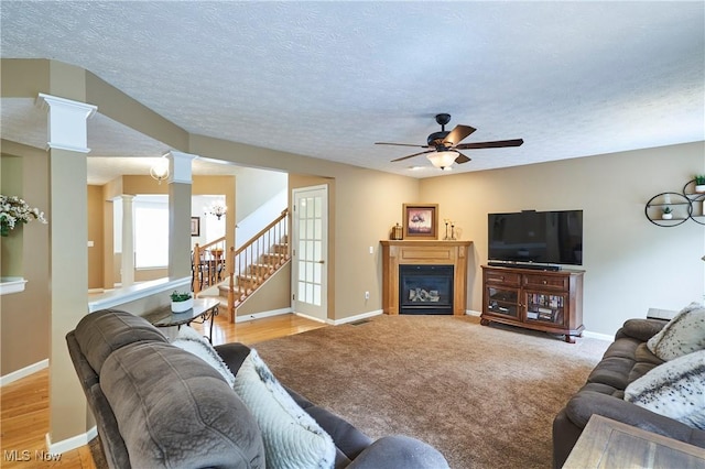 living room featuring a ceiling fan, ornate columns, a fireplace, stairway, and a textured ceiling
