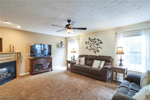 living room with healthy amount of natural light, carpet flooring, ceiling fan, a glass covered fireplace, and a textured ceiling