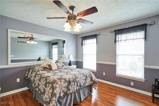 bedroom with multiple windows, wood finished floors, a textured ceiling, and a ceiling fan