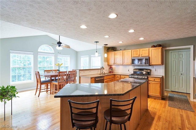 kitchen featuring appliances with stainless steel finishes, a ceiling fan, light wood-style floors, a peninsula, and a textured ceiling