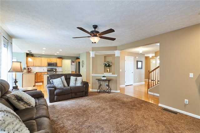 living room featuring light colored carpet, a ceiling fan, decorative columns, stairway, and a textured ceiling