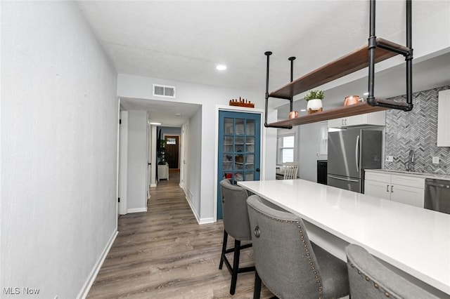 908 Dawnwood Dr, Parma, OH 44134 - kitchen with stainless steel appliances, decorative backsplash, white cabinets, wood finished floors, and a kitchen breakfast bar