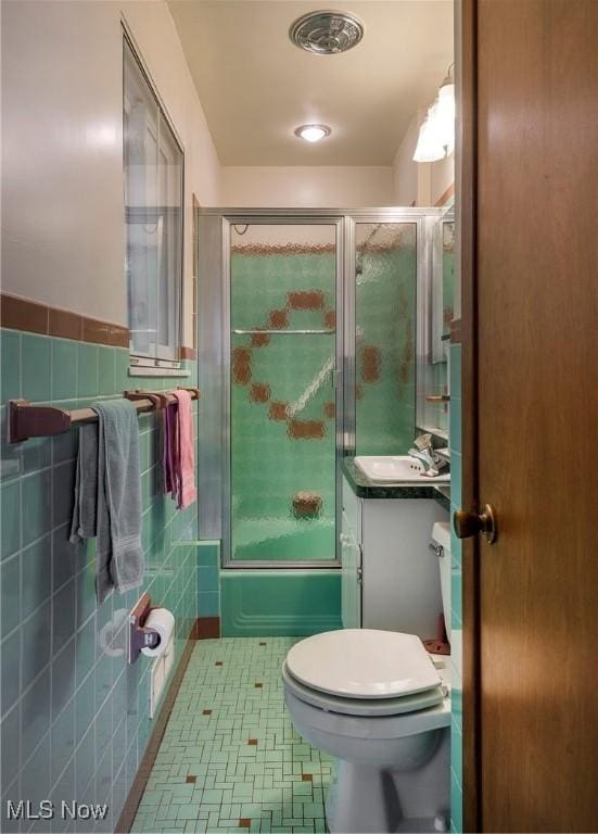 7080 Arcadia Dr, Parma, OH 44129 - bathroom featuring bath / shower combo with glass door, vanity, tile walls, and a wainscoted wall