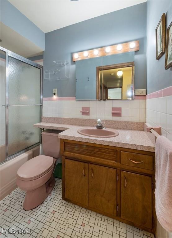 7080 Arcadia Dr, Parma, OH 44129 - bathroom featuring tile walls, vanity, bath / shower combo with glass door, and a wainscoted wall