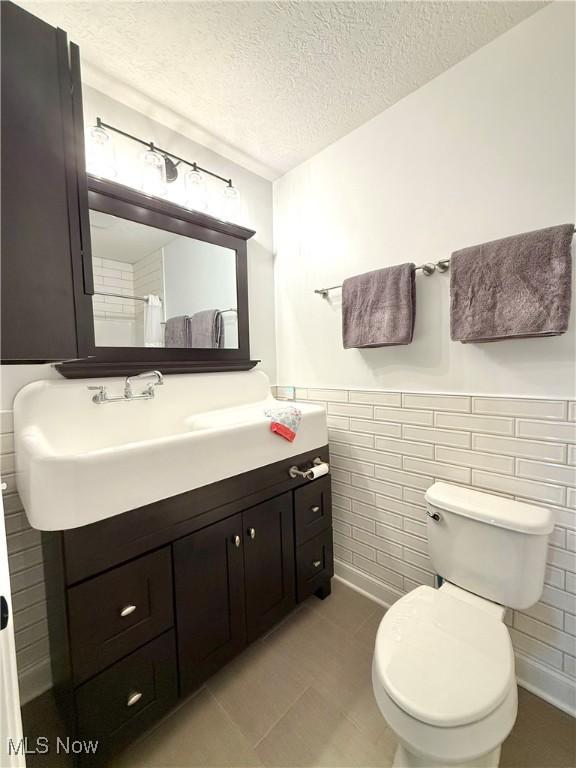 2710 E Hutton Rd, Wooster, OH 44691 - bathroom featuring vanity, tile walls, a textured ceiling, tile patterned floors, and a wainscoted wall