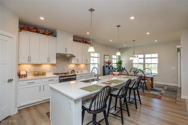 34674 N Legends Way, Grafton, OH 44044 - kitchen with electric stove, under cabinet range hood, backsplash, light wood-style flooring, and an island with sink