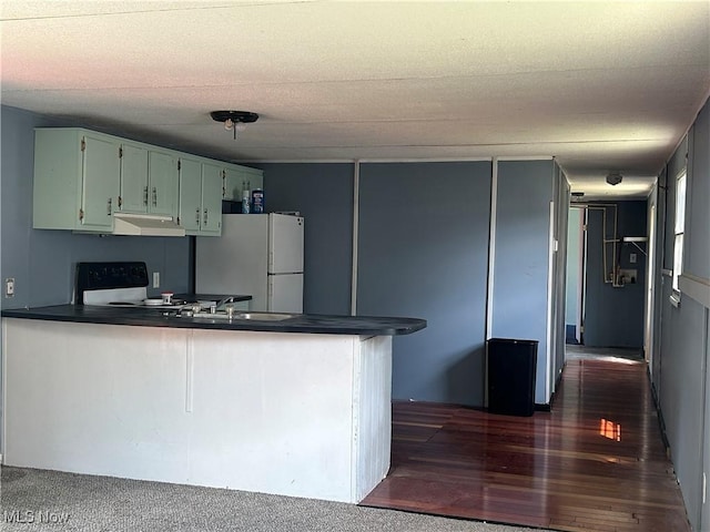 152 N Main St Unit 2, New London, OH 44851 - kitchen with freestanding refrigerator, dark countertops, a peninsula, under cabinet range hood, and dark wood-type flooring