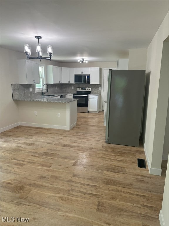 9822 Hooper Rd, Athens, OH 45701 - kitchen with appliances with stainless steel finishes, a peninsula, white cabinets, a chandelier, and tasteful backsplash