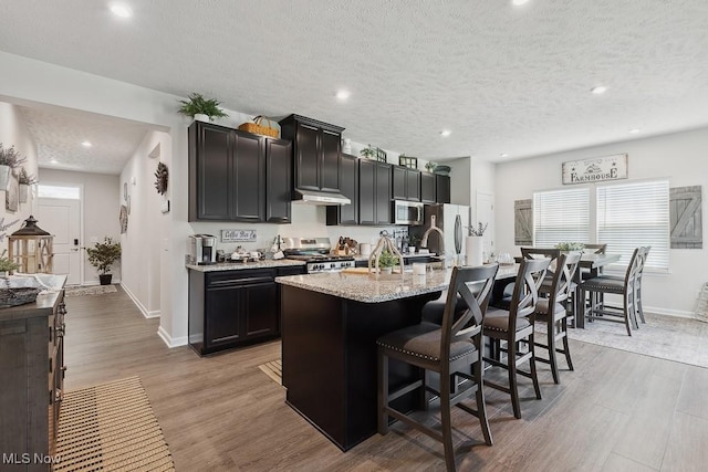 2014 Sugar Maple Dr, Kent, OH 44240 - kitchen with stainless steel appliances, a kitchen island with sink, a kitchen bar, a textured ceiling, and light wood-type flooring