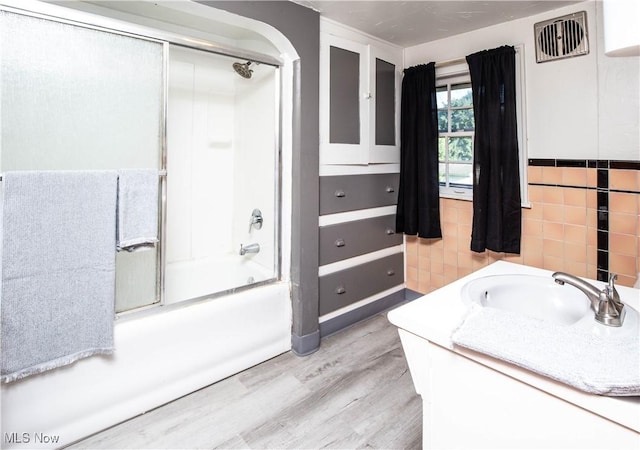 1299 Herberich Ave, Akron, OH 44301 - bathroom with bath / shower combo with glass door, wood finished floors, vanity, tile walls, and a wainscoted wall