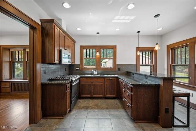 159 Edgerton Rd, Akron, OH 44303 - kitchen featuring range with gas stovetop, stainless steel microwave, radiator heating unit, backsplash, and a peninsula