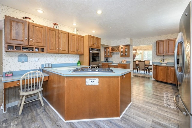 3043 E Wallings Rd, Broadview Heights, OH 44147 - kitchen with wallpapered walls, appliances with stainless steel finishes, brown cabinets, light wood finished floors, and a peninsula