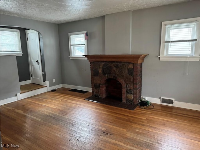 667 Eastland Ave, Akron, OH 44305 - unfurnished living room featuring hardwood / wood-style flooring, a textured ceiling, arched walkways, and a fireplace with flush hearth