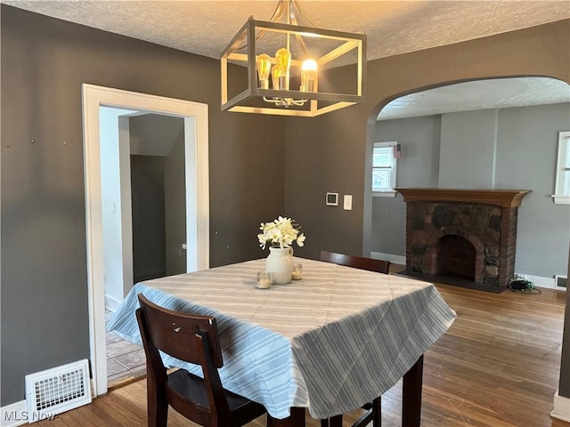 667 Eastland Ave, Akron, OH 44305 - dining room with arched walkways, a chandelier, wood finished floors, a stone fireplace, and a textured ceiling