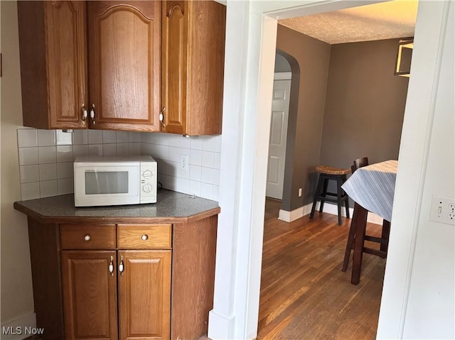 667 Eastland Ave, Akron, OH 44305 - kitchen with white microwave, arched walkways, dark countertops, dark wood finished floors, and brown cabinets