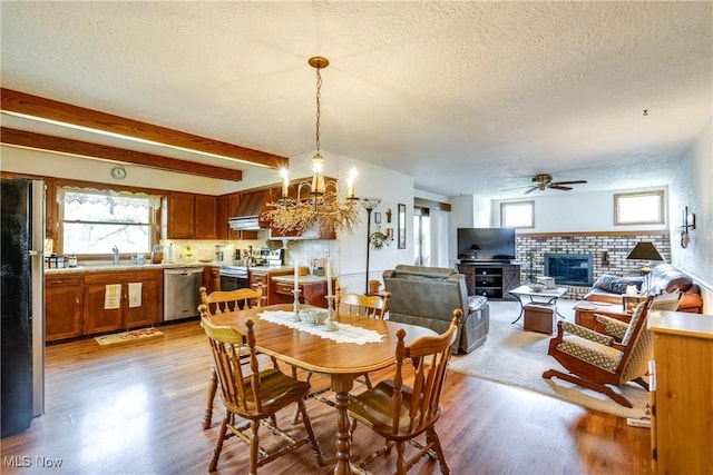 10154 Carlswood Ave NE, Hartville, OH 44632 - dining room featuring ceiling fan, light wood-style floors, a textured ceiling, a brick fireplace, and healthy amount of natural light