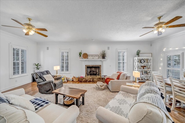 living room with crown molding, a textured ceiling, light wood-type flooring, a premium fireplace, and ceiling fan