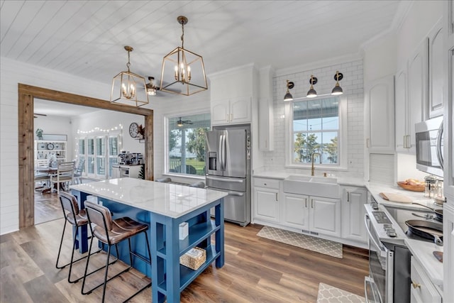 kitchen featuring appliances with stainless steel finishes, white cabinets, a kitchen island, sink, and backsplash