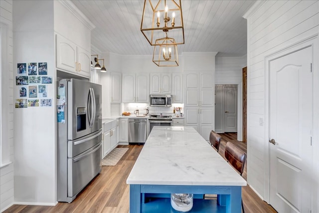 kitchen featuring light stone countertops, pendant lighting, white cabinets, appliances with stainless steel finishes, and a chandelier