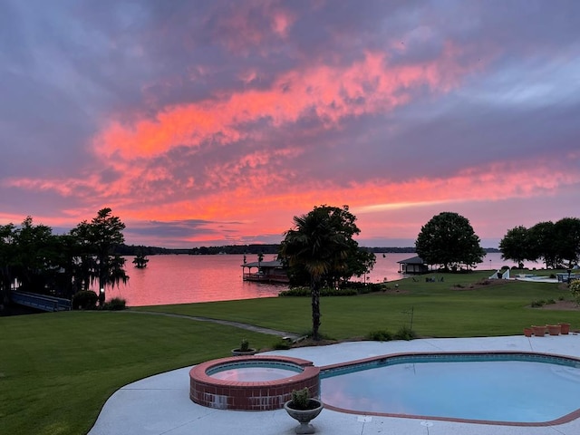 pool at dusk featuring an in ground hot tub, a yard, and a water view