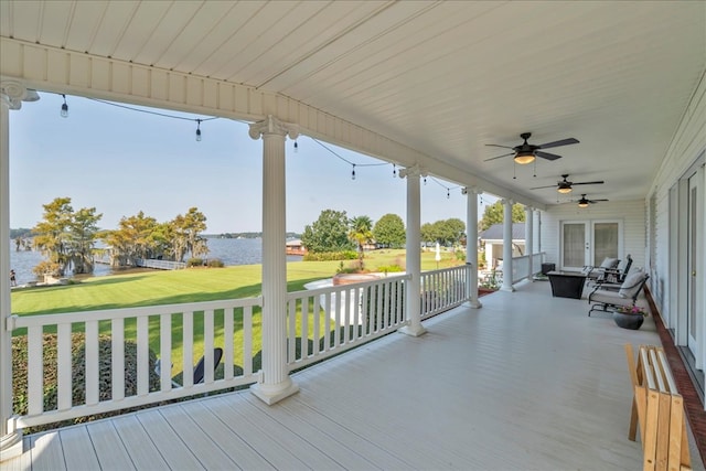 wooden deck with ceiling fan, a water view, and a yard