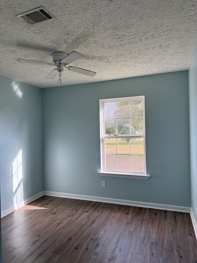 spare room featuring a textured ceiling, dark wood-style flooring, visible vents, and baseboards