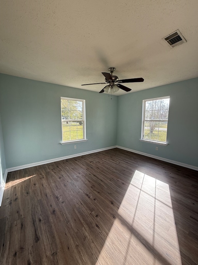 unfurnished room featuring plenty of natural light, wood finished floors, visible vents, and baseboards