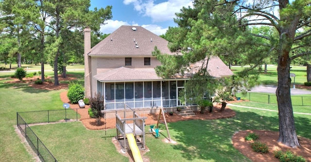 rear view of property with a sunroom, a lawn, and a playground