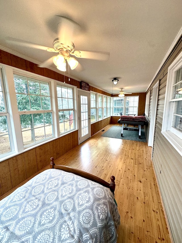 bedroom with ceiling fan, multiple windows, and wood walls