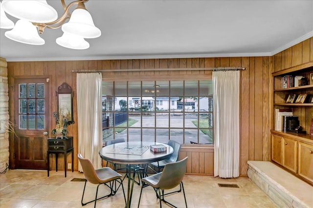 dining room featuring light tile patterned floors, ornamental molding, a chandelier, and wooden walls