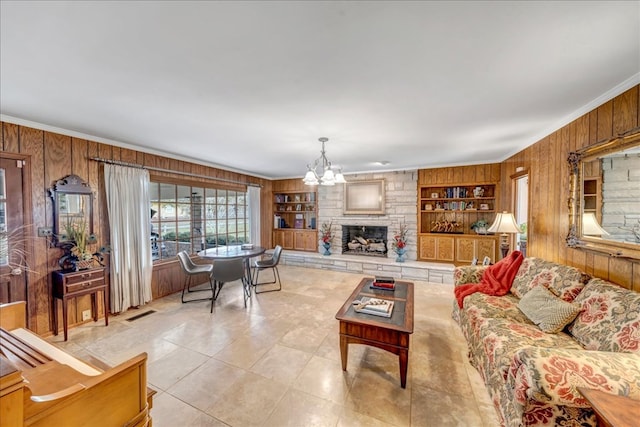 living room with crown molding, built in features, a fireplace, wood walls, and an inviting chandelier