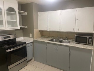 kitchen featuring appliances with stainless steel finishes, white cabinetry, light tile patterned floors, sink, and light stone counters