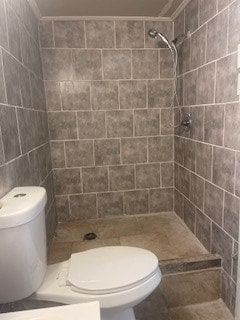 bathroom with toilet, tiled shower, and tile walls