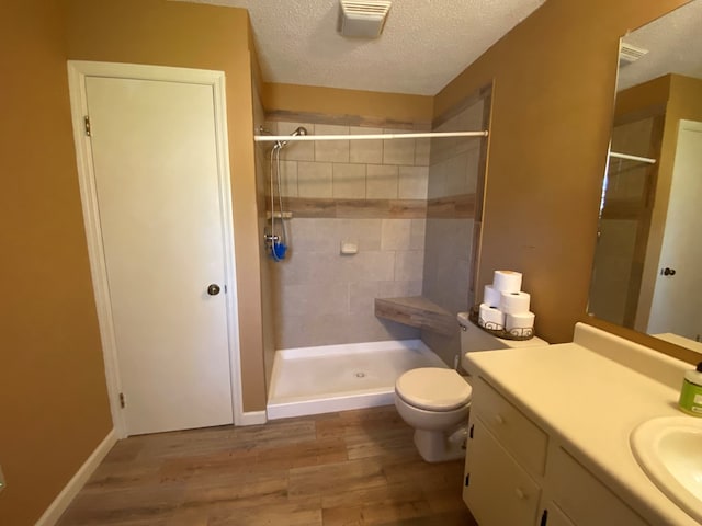 bathroom with tiled shower, vanity, wood-type flooring, a textured ceiling, and toilet