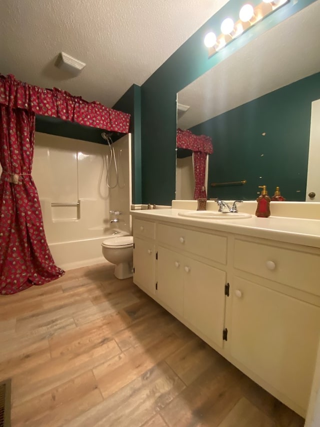 full bathroom featuring hardwood / wood-style flooring,  shower combination, vanity, a textured ceiling, and toilet