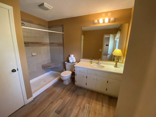 bathroom with a tile shower, hardwood / wood-style flooring, vanity, toilet, and a textured ceiling