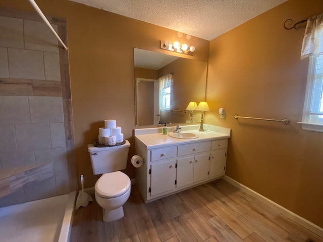 bathroom featuring wood-type flooring, a shower, vanity, toilet, and a textured ceiling