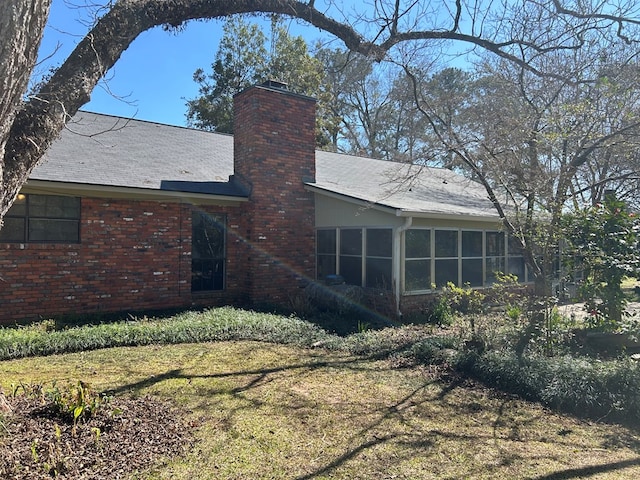 back of property featuring a yard, a sunroom, a chimney, and brick siding